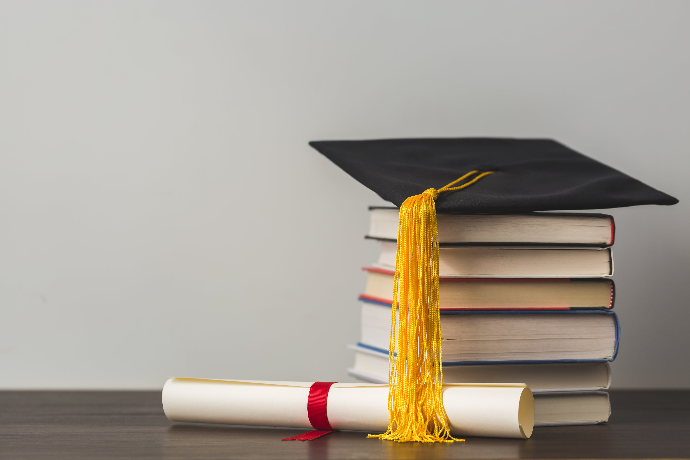 Textbooks stacked with a graduation cap and diploma sitting nearby