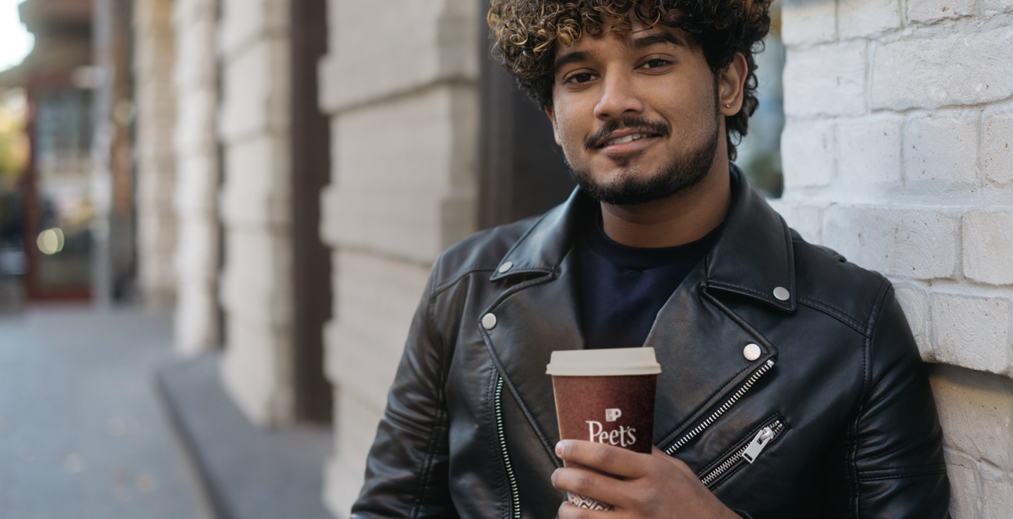 Man in leather jacket holding Peet's to-go cup outside brick building